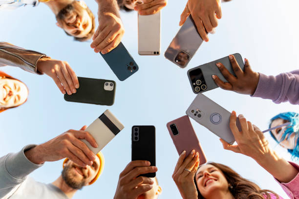 Group of diverse people holding smartphones in a circular formation viewed from above, showcasing various phone models and cases